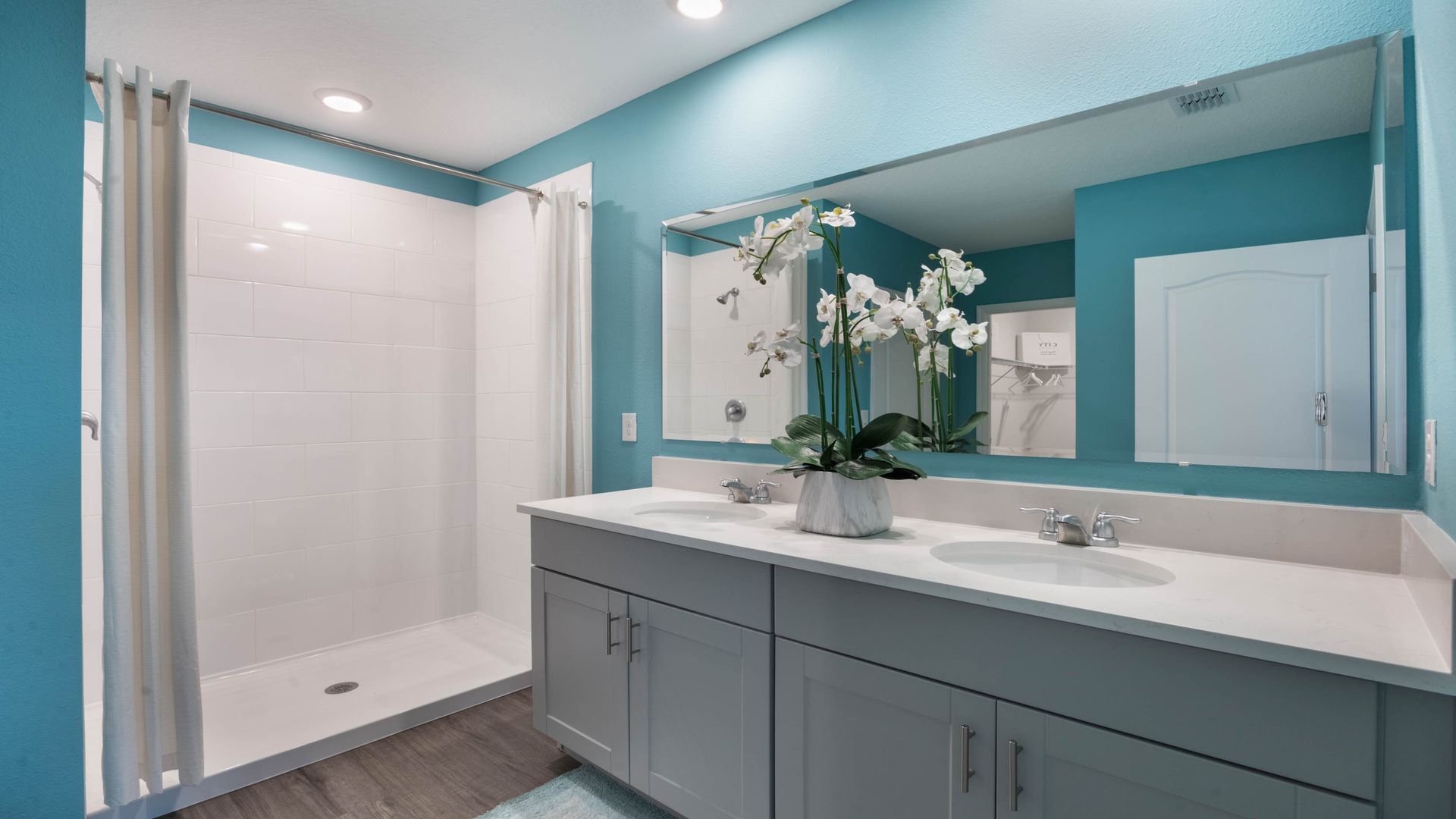 Modern bathroom with double vanity, large wall mirror, cabinets and quartz countertops along with walk-in shower