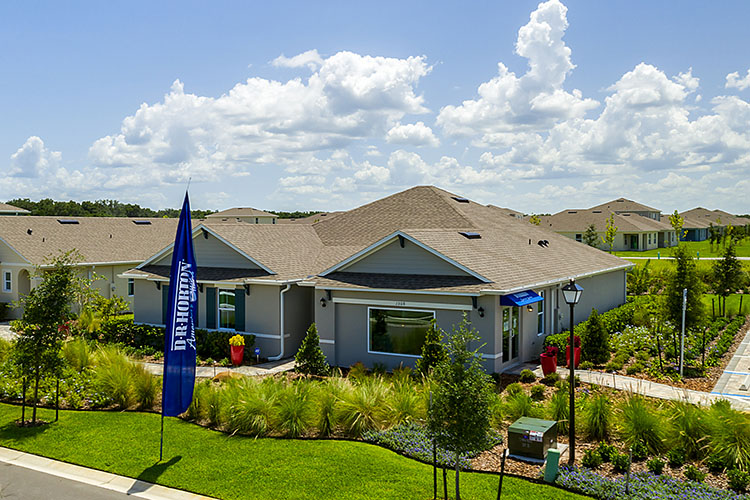 Arial view of single story new home with driveway, large windows, and grassy front yard.