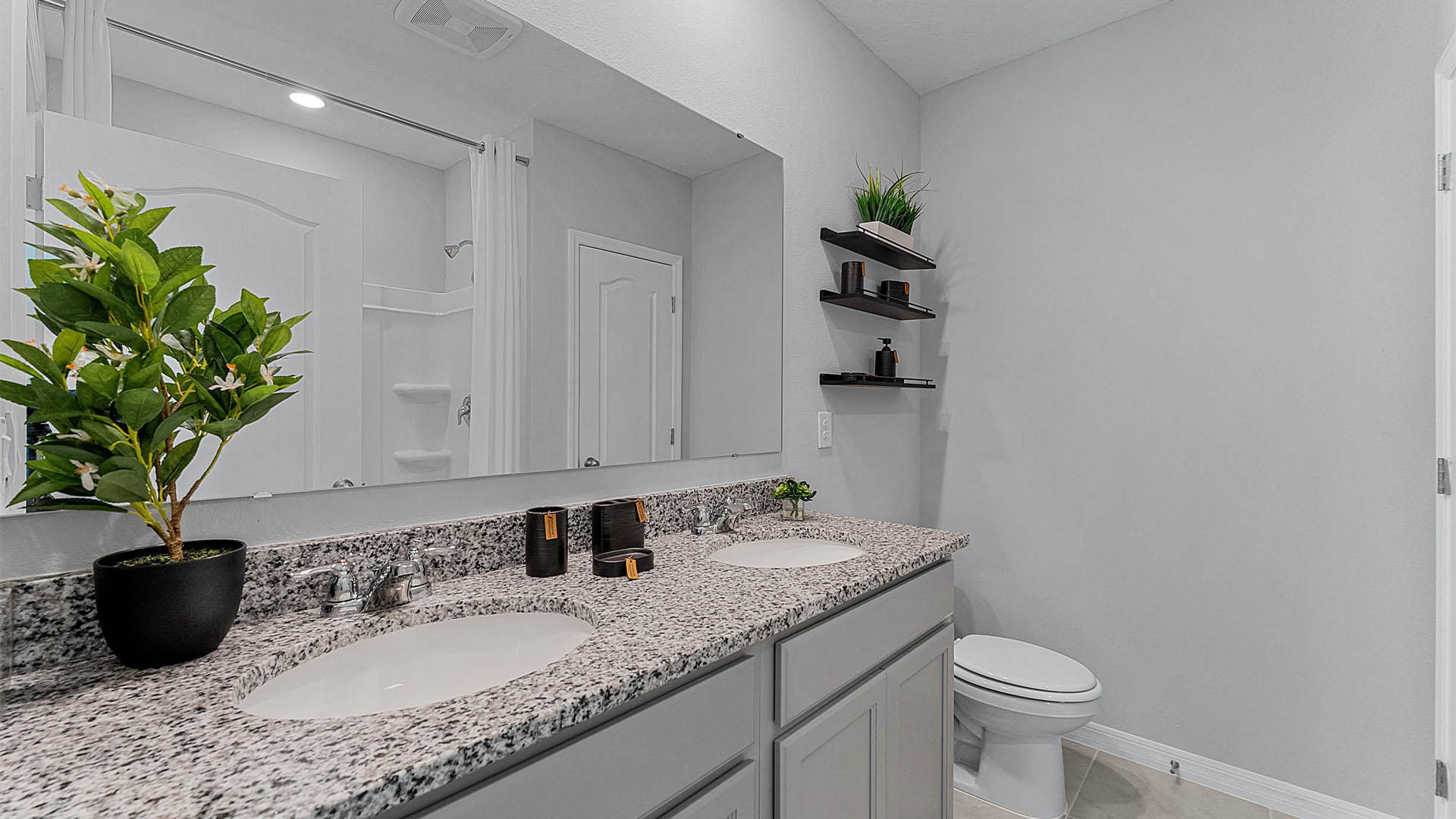Modern bathroom with double vanity, large wall mirror, cabinets and granite countertops along with toilet and shower