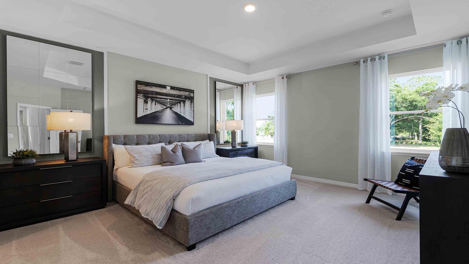 Spacious primary bedroom with king size bed, carpet flooring, natural lighting overseeing living area.