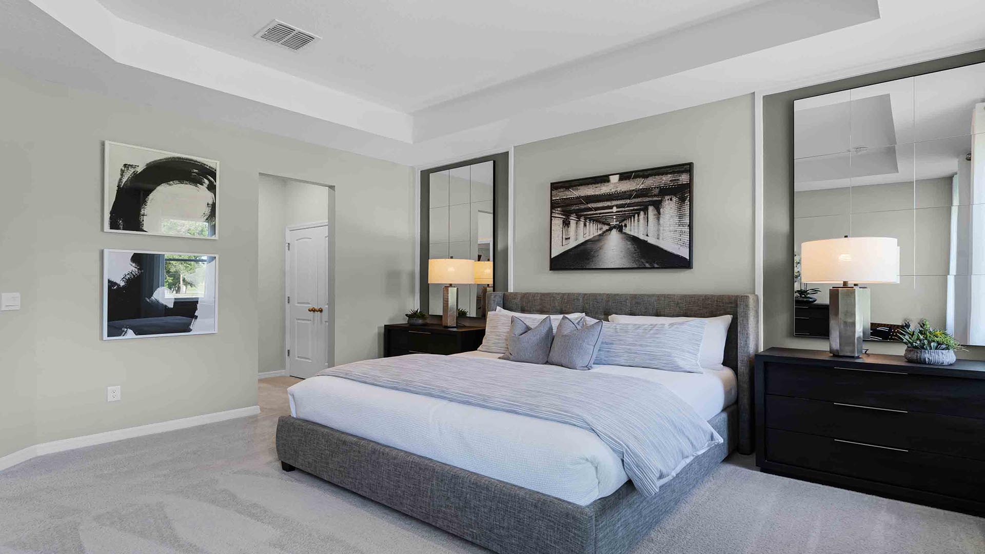 Spacious primary bedroom with king size bed, carpet flooring, natural lighting overseeing living area with access to master bathroom.