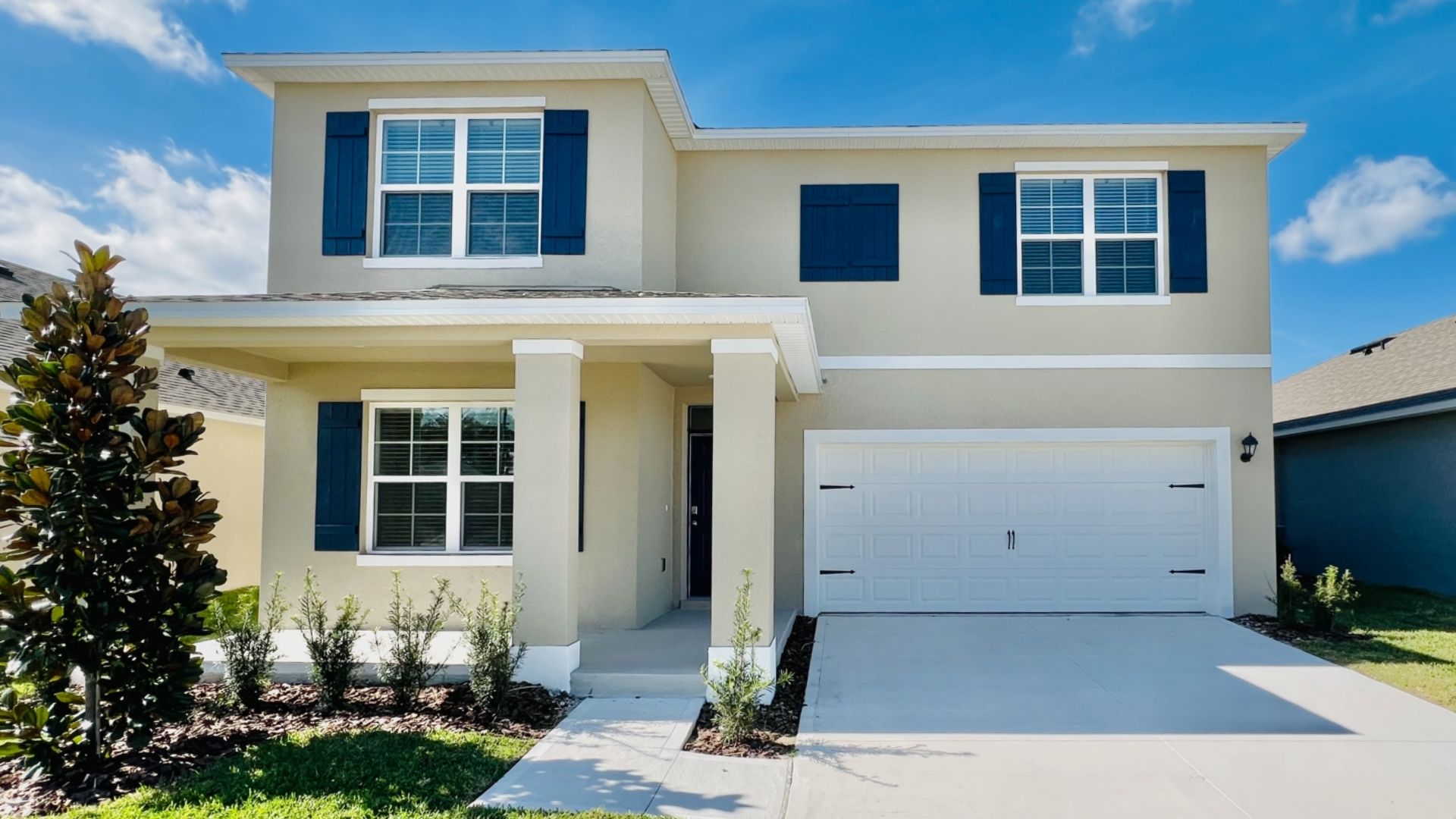 Two-story new home with driveway, large windows, and grassy front yard.