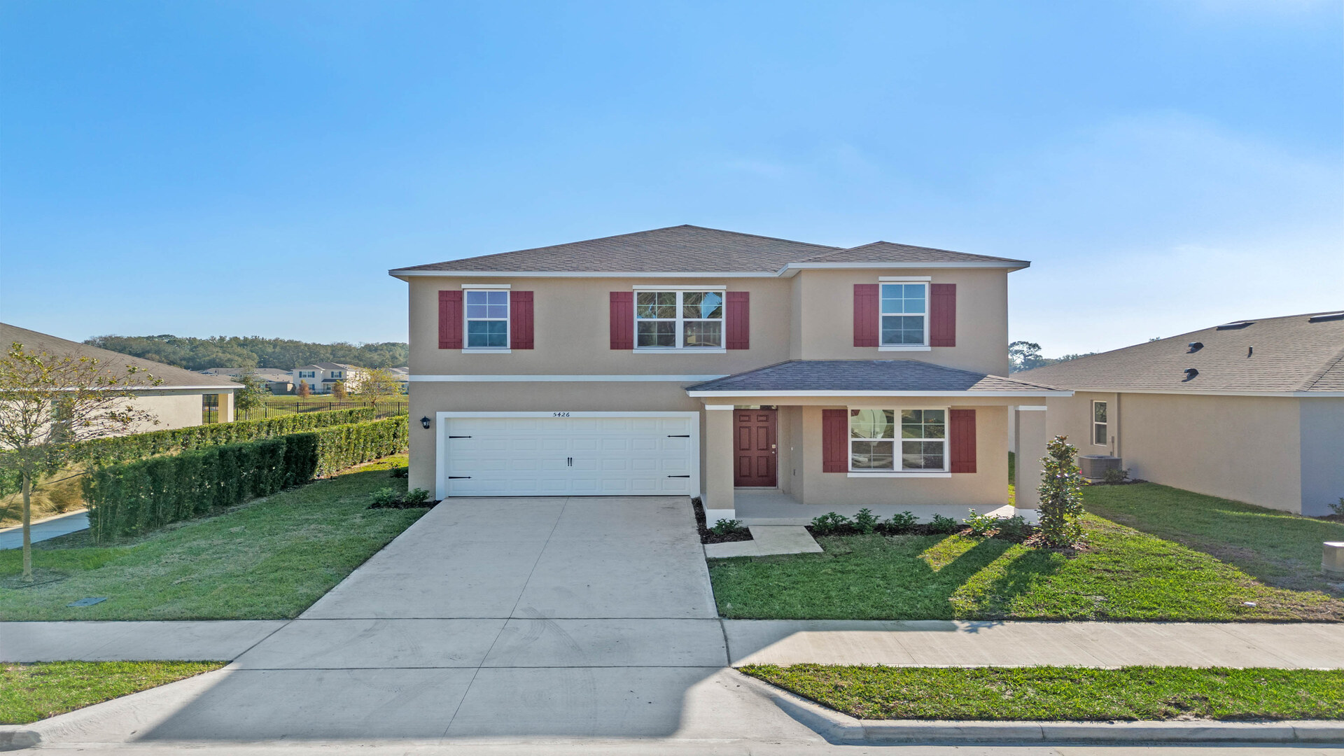 Two-story new home with driveway, large windows, and grassy front yard.