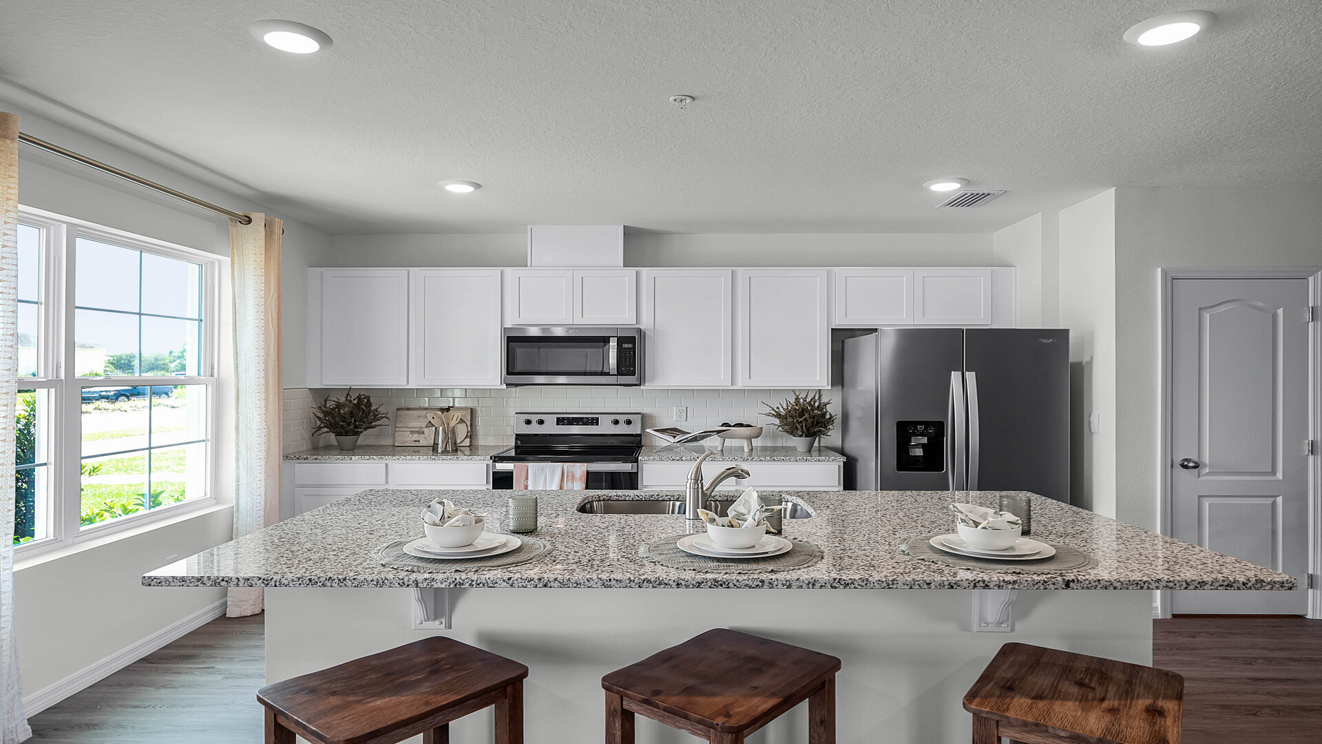 Kitchen with island seating, granite counters, spacous pantry and stainless steel appliances.