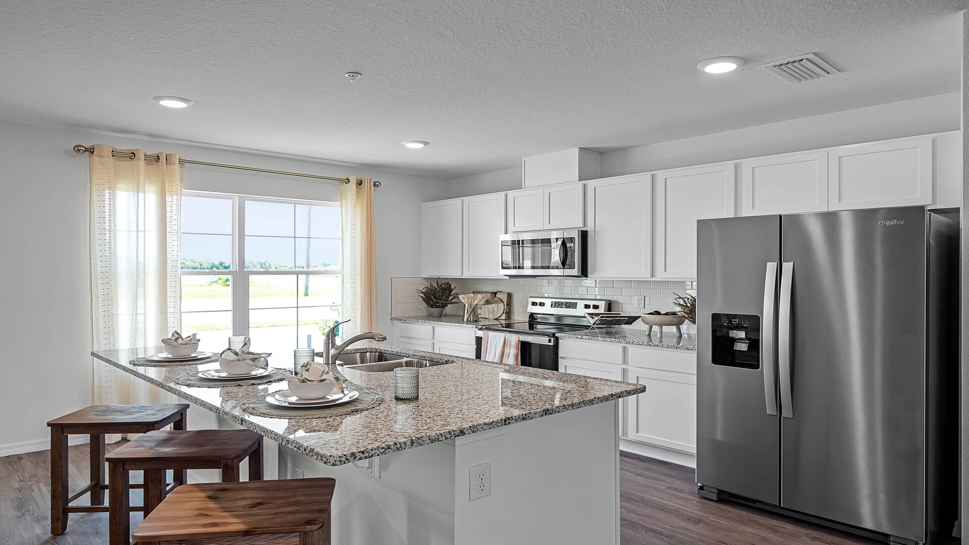 Kitchen with island seating, granite counters, spacous pantry and stainless steel appliances.