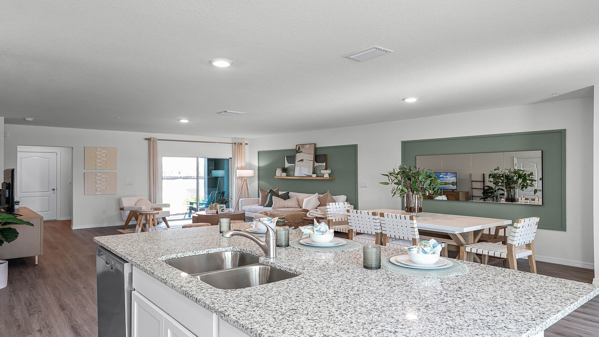Kitchen with island seating, granite counters, spacous pantry and stainless steel appliances overseeing dining room and living area.