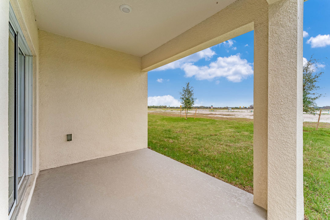 Rear of home with view of grassed backyard, porch seating and slider glass doors.