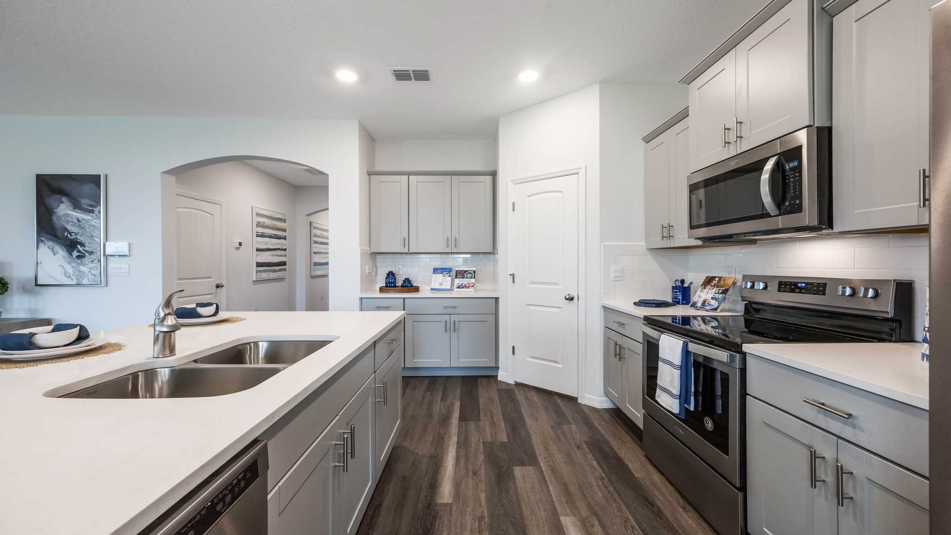 Kitchen with island seating, quartz counters, spacious pantry and stainless steel appliances showing entry way to home overseeing living area.