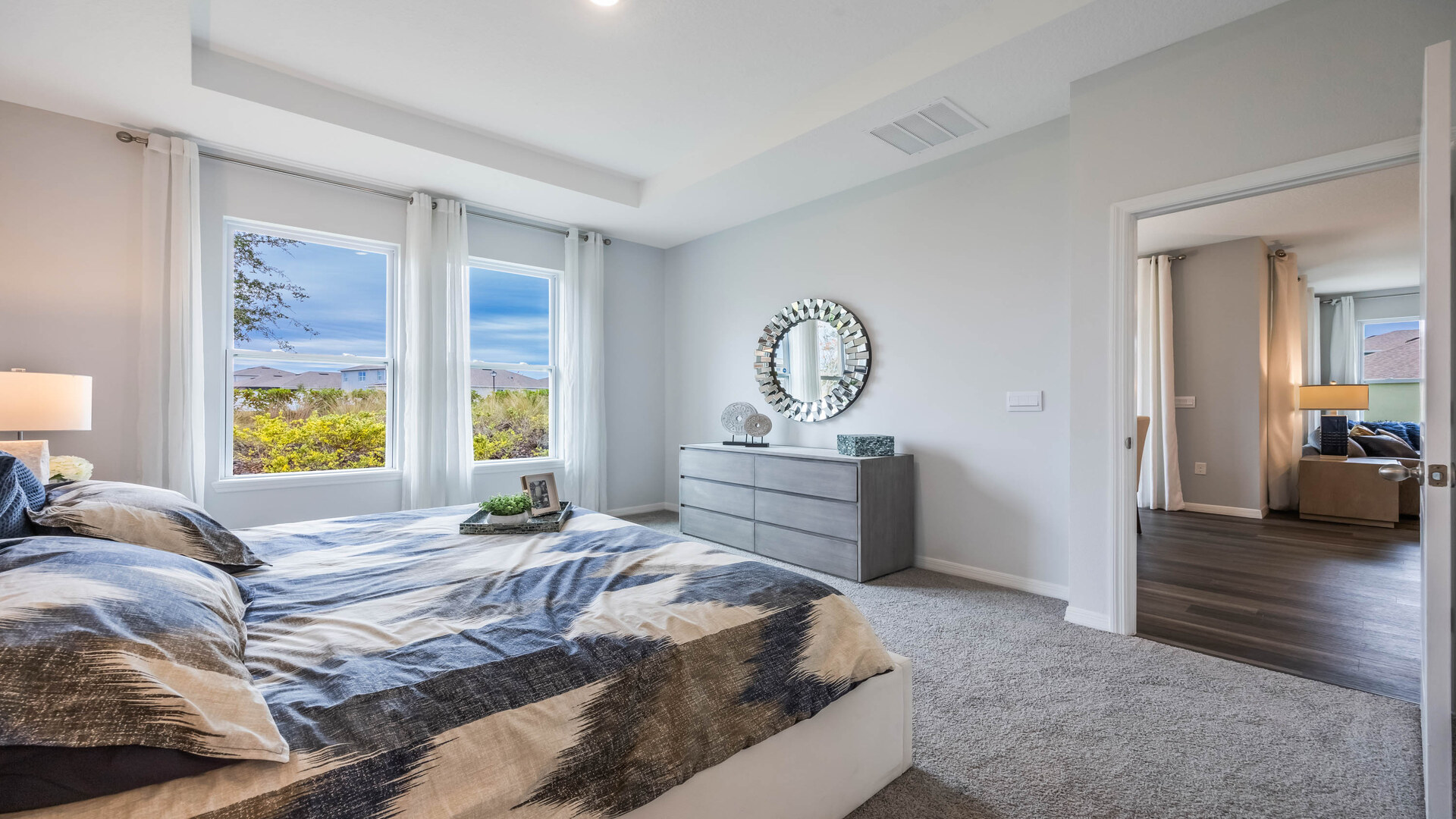 Spacious primary bedroom with king size bed, carpet flooring, natural lighting.