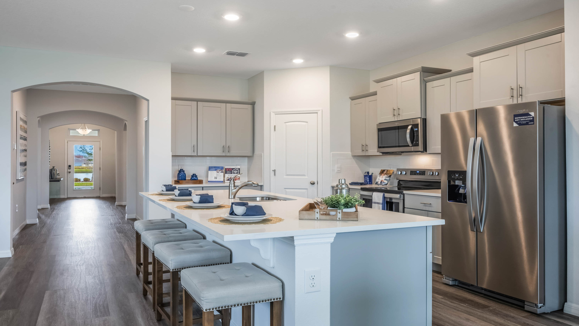 Kitchen with island seating, quartz counters, spacious pantry and stainless steel appliances showing entry way to home overseeing primary bedroom