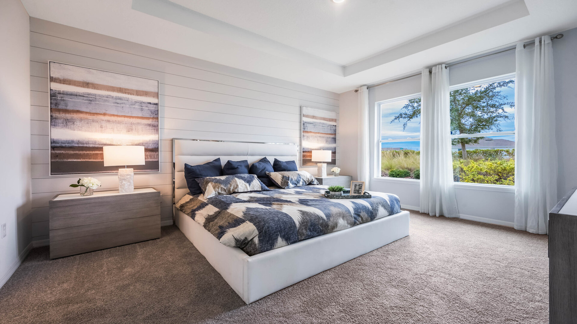 Spacious primary bedroom with king size bed, carpet flooring, natural lighting.