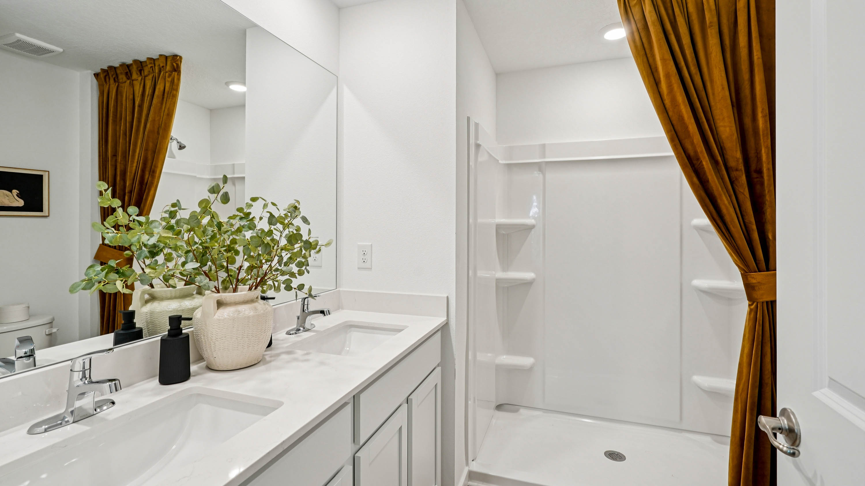 Modern bathroom with double vanity, large wall mirror, cabinets and quartz countertops along with toilet and walk-in shower