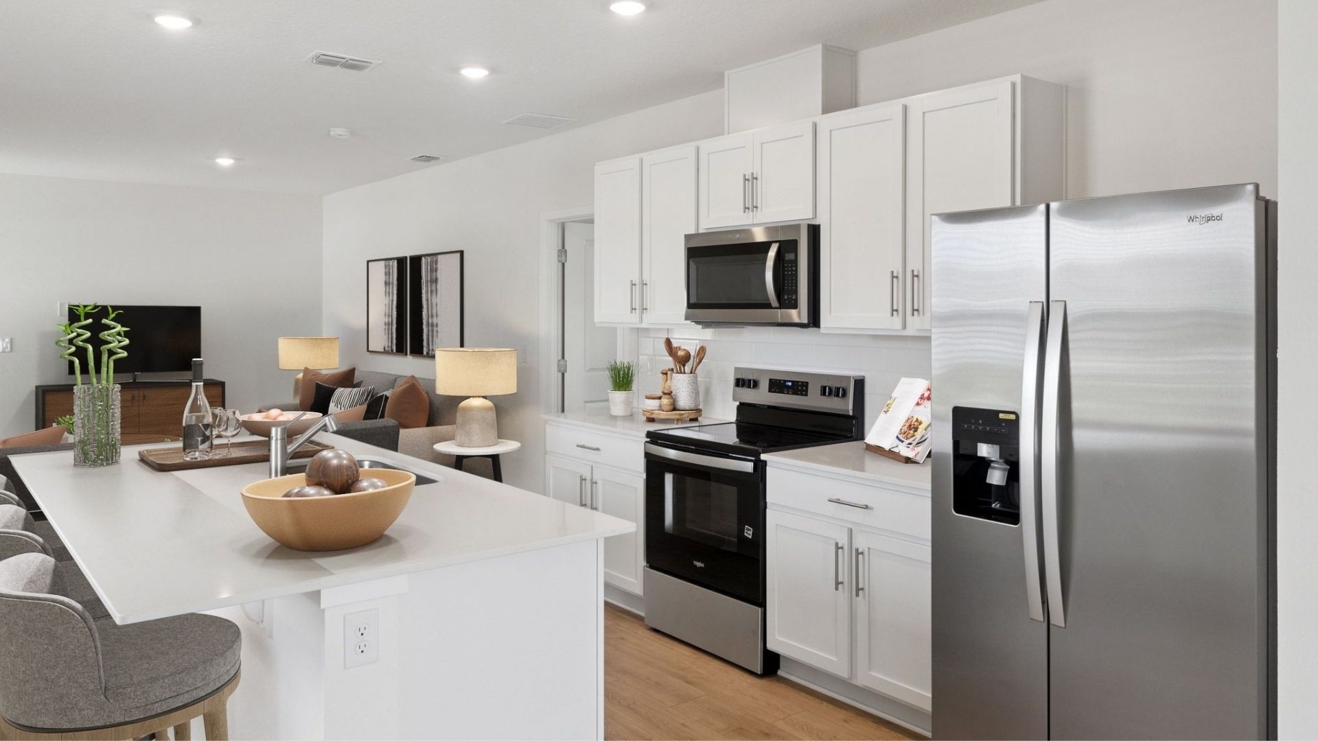 Kitchen with island seating, quartz counters, spacious pantry and stainless steel appliances overseeing living area.