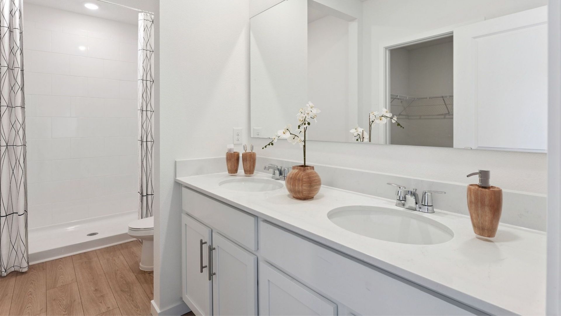 Modern bathroom with double vanity, large wall mirror, cabinets and quartz countertops along with toilet and walk-in shower