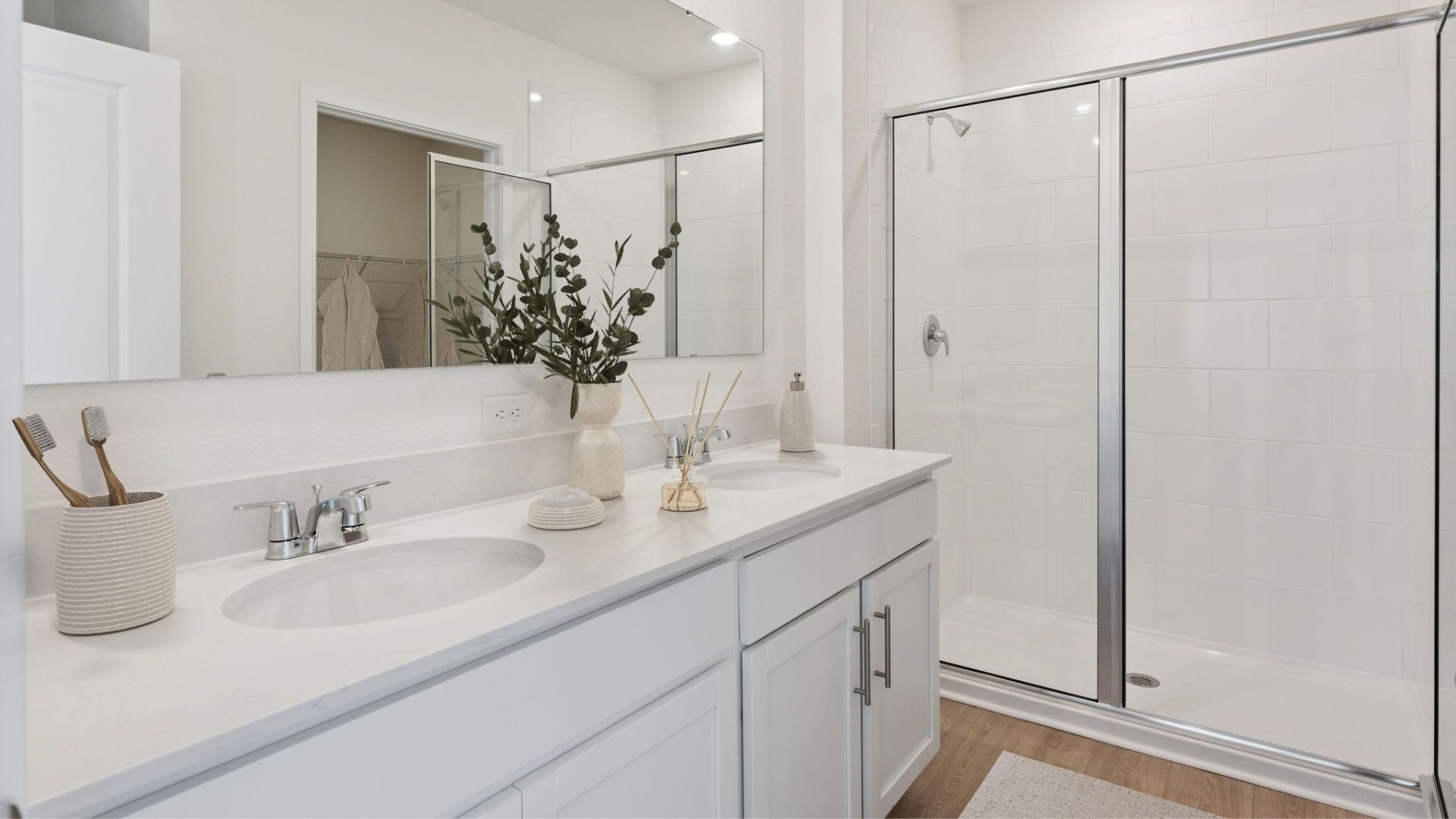 Modern bathroom with double vanity, large wall mirror, cabinets and quartz countertops along with walk-in shower