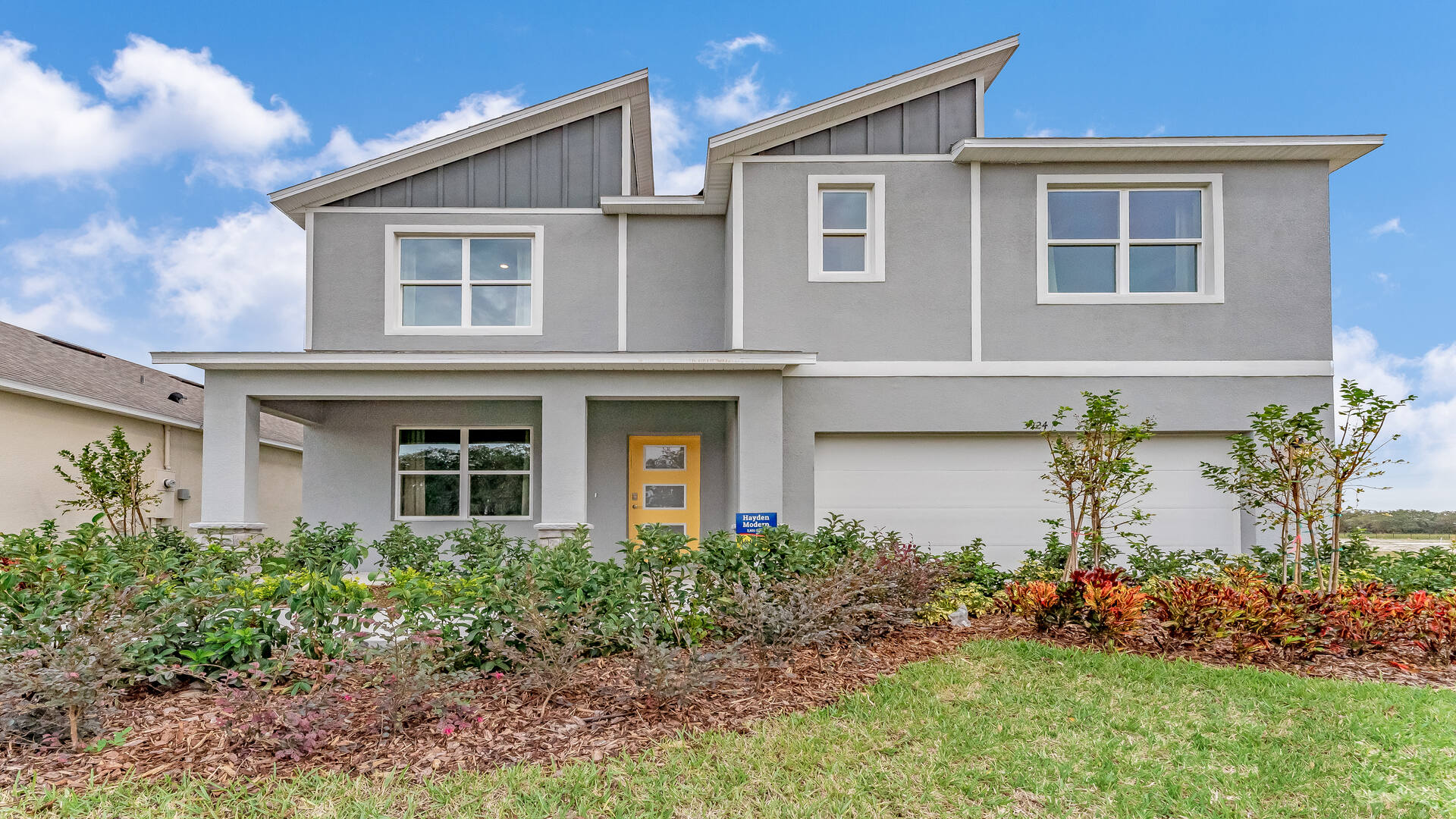 Two-story new home with driveway, large windows, and grassy front yard.
