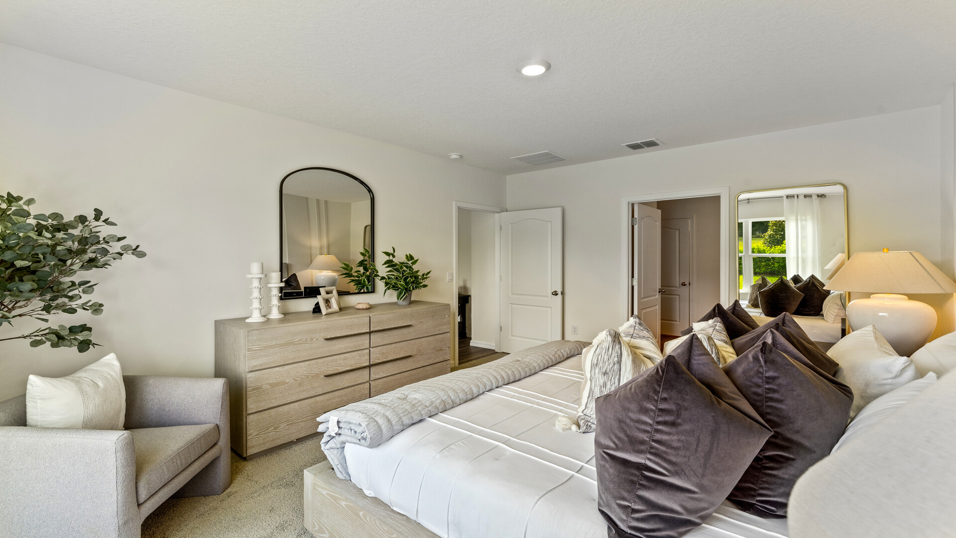 Spacious primary bedroom with king size bed, carpet flooring, natural lighting.