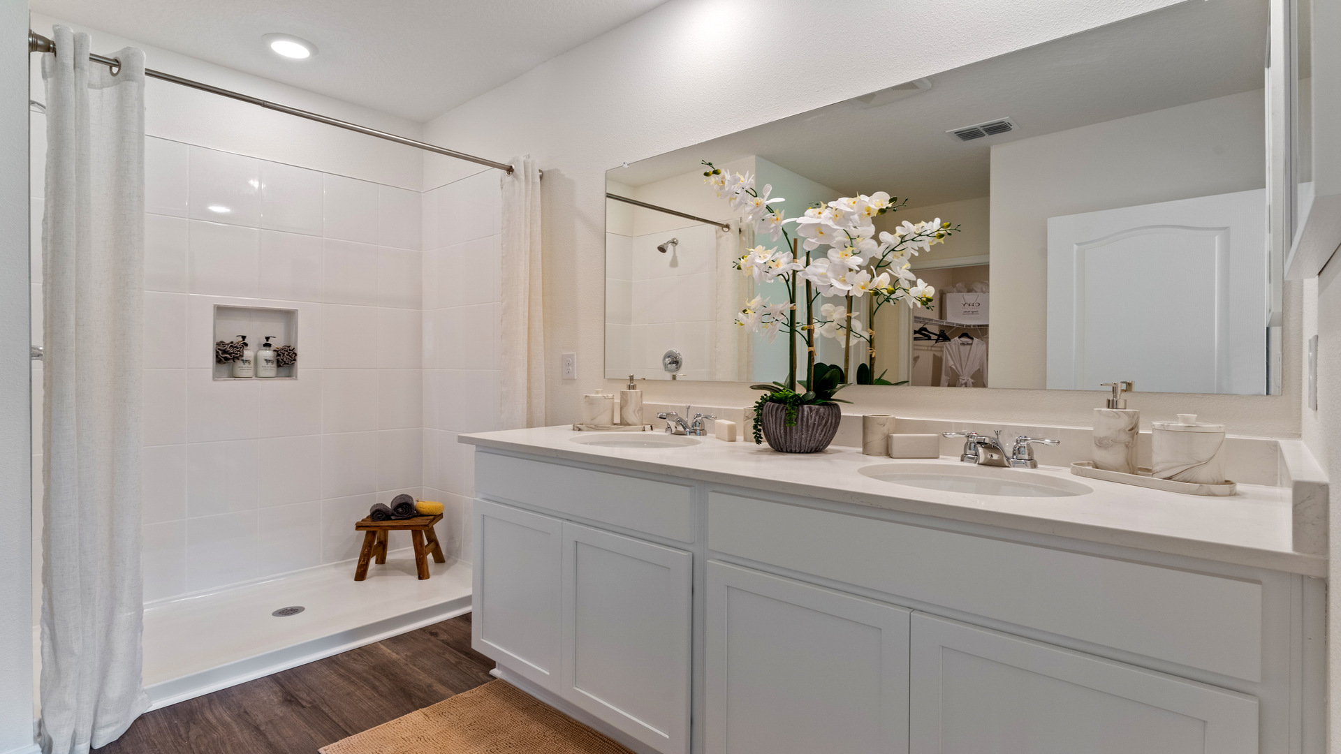 Modern bathroom with double vanity, large wall mirror, cabinets and quartz countertops along with walk-in shower
