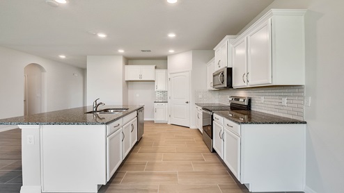 Kitchen with island seating, quartz counters, spacous pantry and stainless steel appliances.