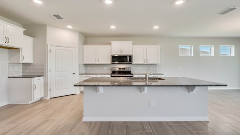Kitchen with island seating, quartz counters, spacous pantry and stainless steel appliances.