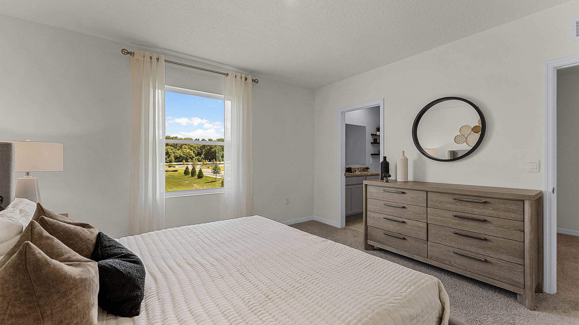 Spacious primary bedroom with king size bed, carpet flooring, natural lighting showing access to walk-in closet and master bathroom.