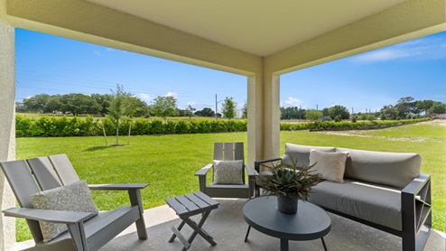 Rear of home with view of grassed backyard, porch seating and slider glass doors.