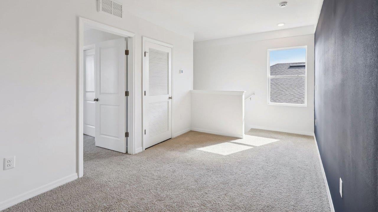 Unfurnished loft space with accent wall and access to primary bedroom
