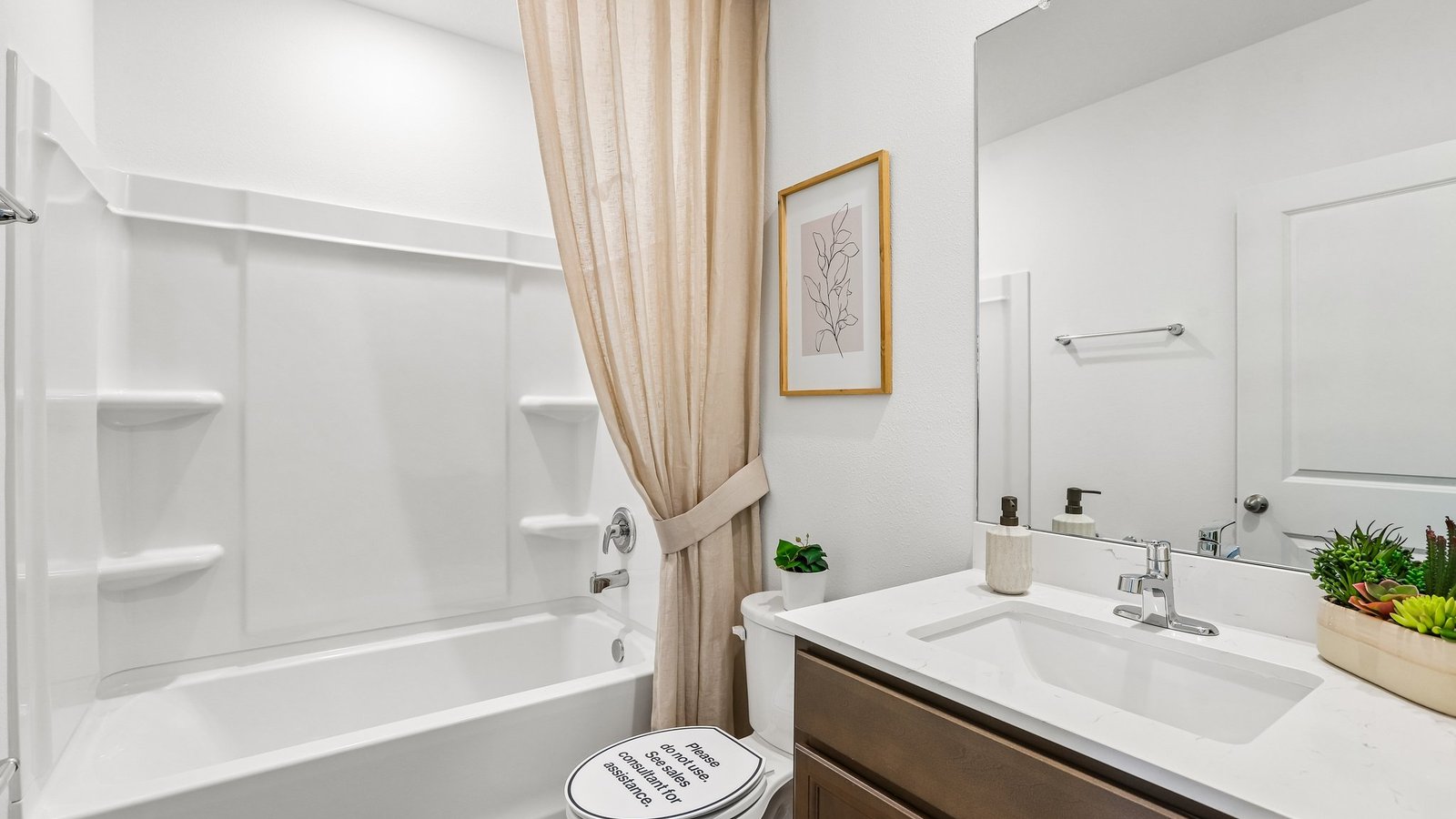 Modern bathroom with single bowl sink, quartz vanity, wall mirror, cabinets and toilet.