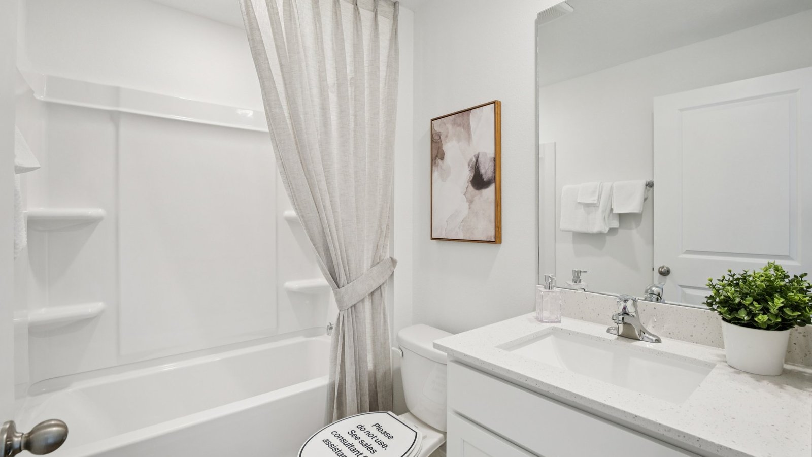 Modern bathroom with single bowl sink, quartz vanity, wall mirror, cabinets and toilet.