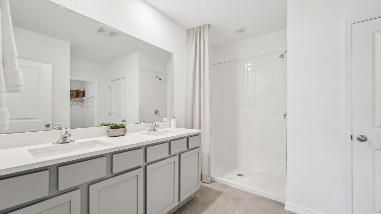 Modern bathroom with double vanity, large wall mirror, cabinets and quartz countertops along with walk-in shower.