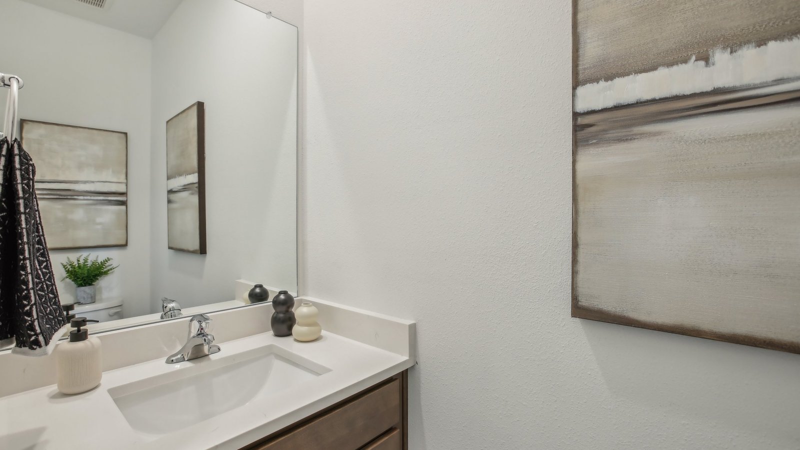 Modern bathroom with single bowl sink, quartz vanity, wall mirror, cabinets and toilet.
