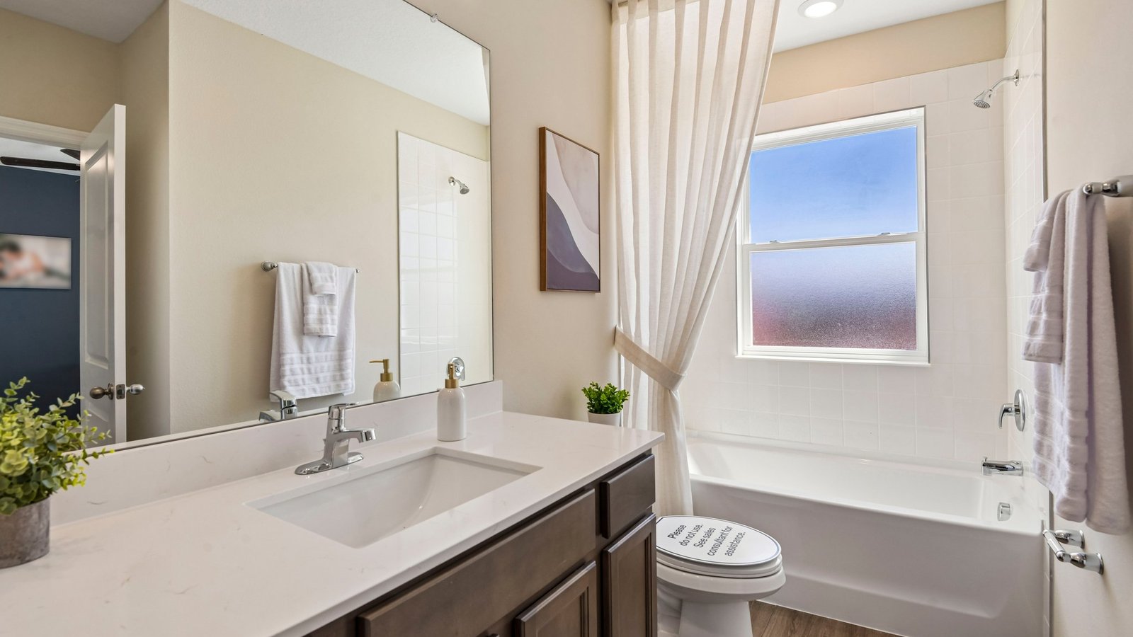 Modern bathroom with single bowl sink, quartz vanity, wall mirror, cabinets and toilet.