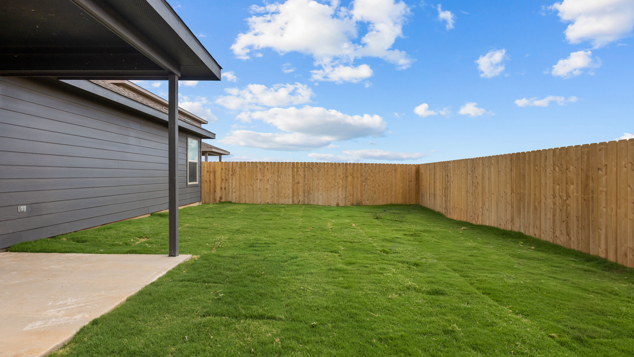 Spacious backyard with green grass, private fence, and covered patio