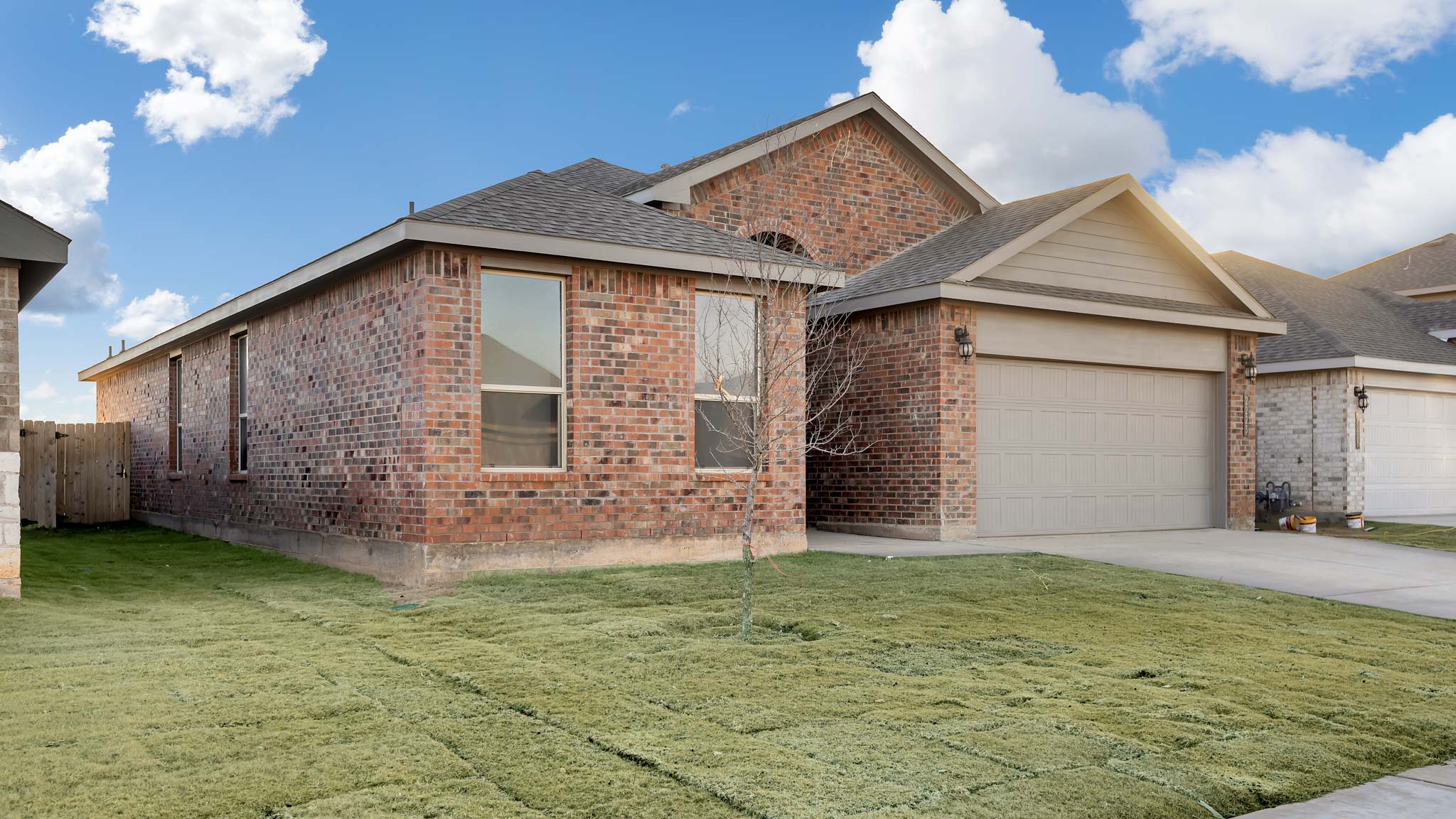 Side view of single- story home with brick, stone, covered patio and two car garage