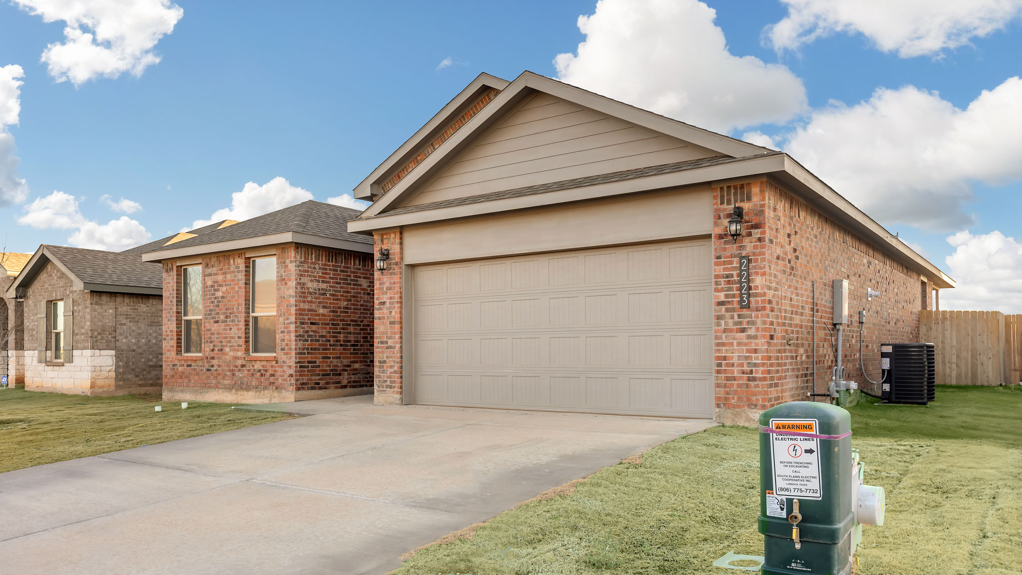 Side view of single- story home with brick, stone, covered patio and two car garage