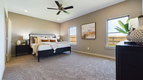 Primary bedroom with plush carpet, attached bathroom and windows overlooking backyard