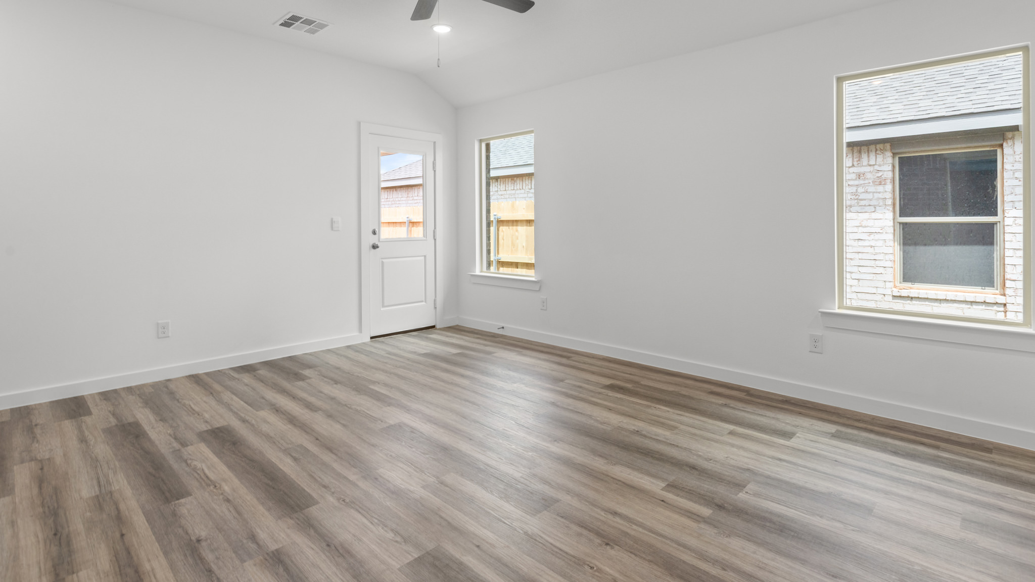 Open airy living room with vinyl plank flooring and windows overlooking the backyard