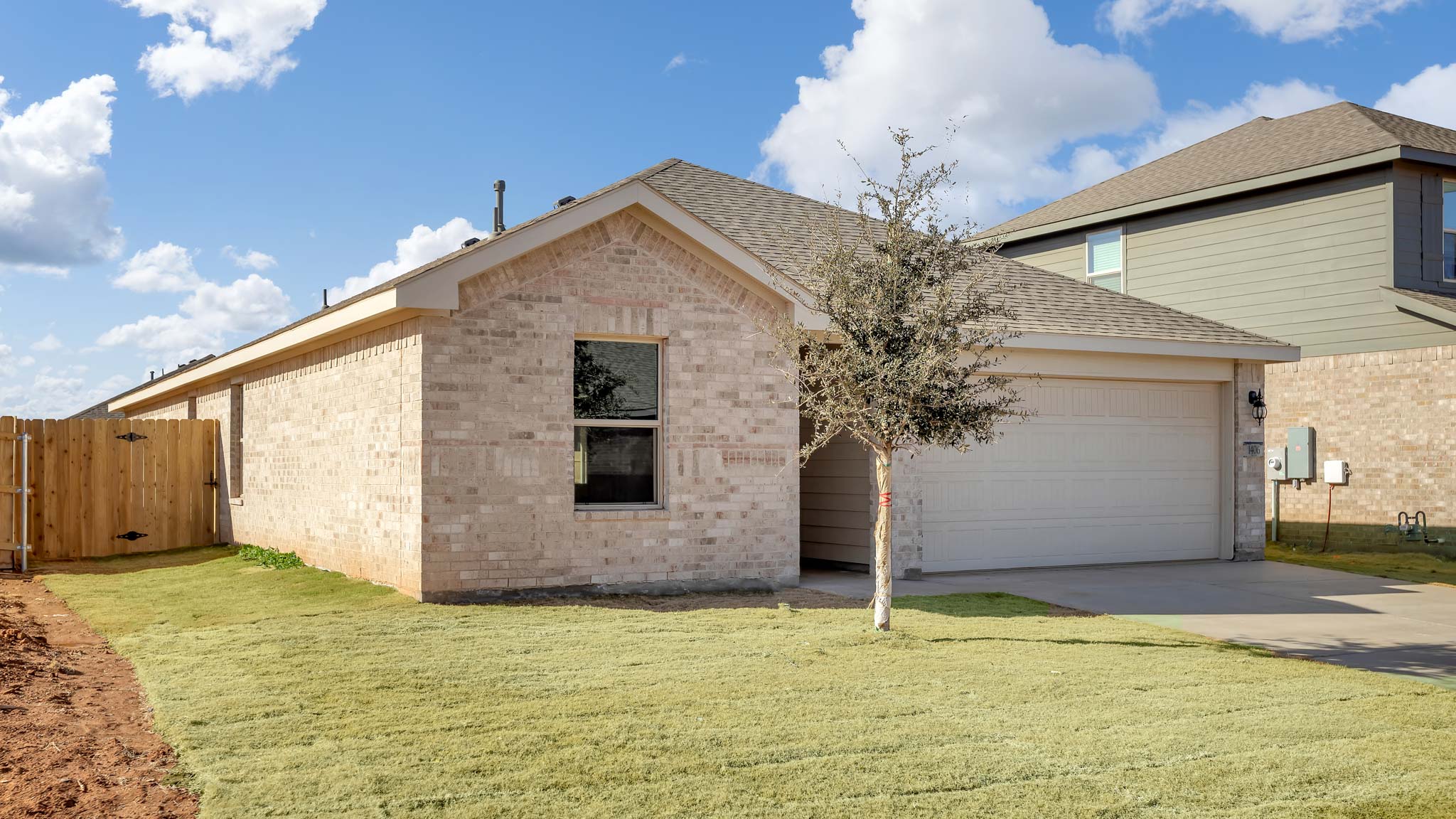 Side view of single- story home with brick, stone, covered patio and two car garage