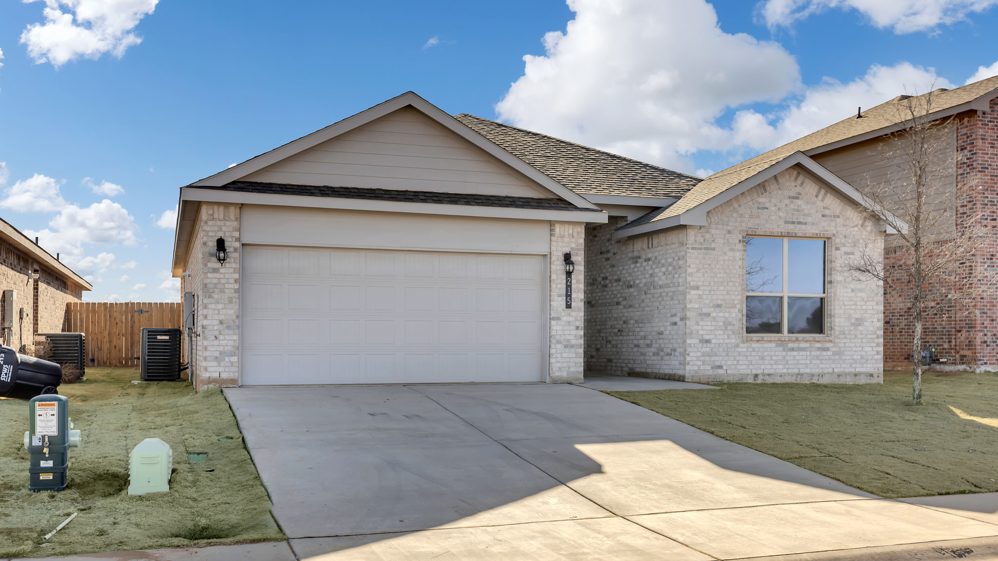Side view of single- story home with brick, stone, covered patio and two car garage