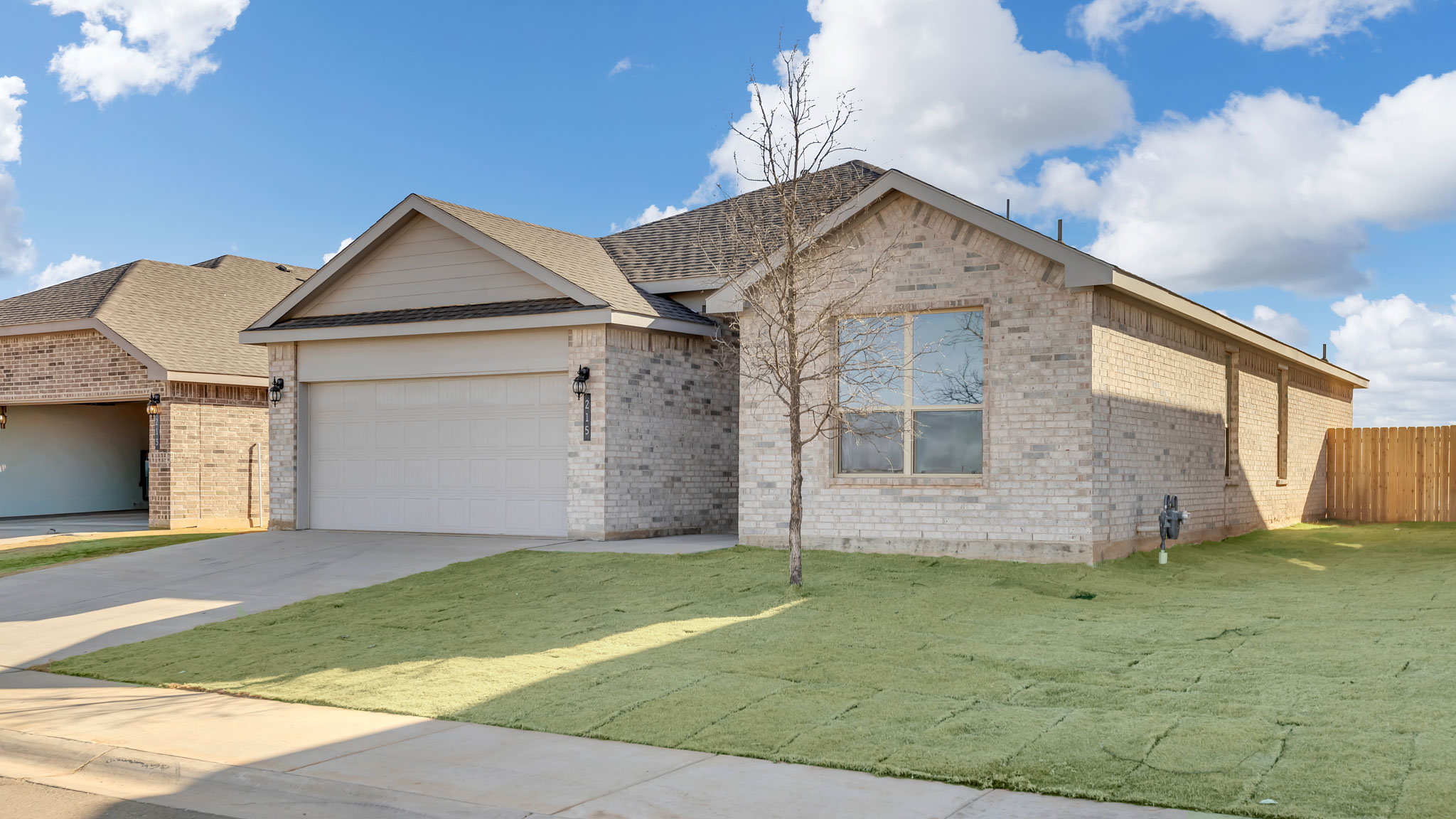 Side view of single- story home with brick, stone, covered patio and two car garage