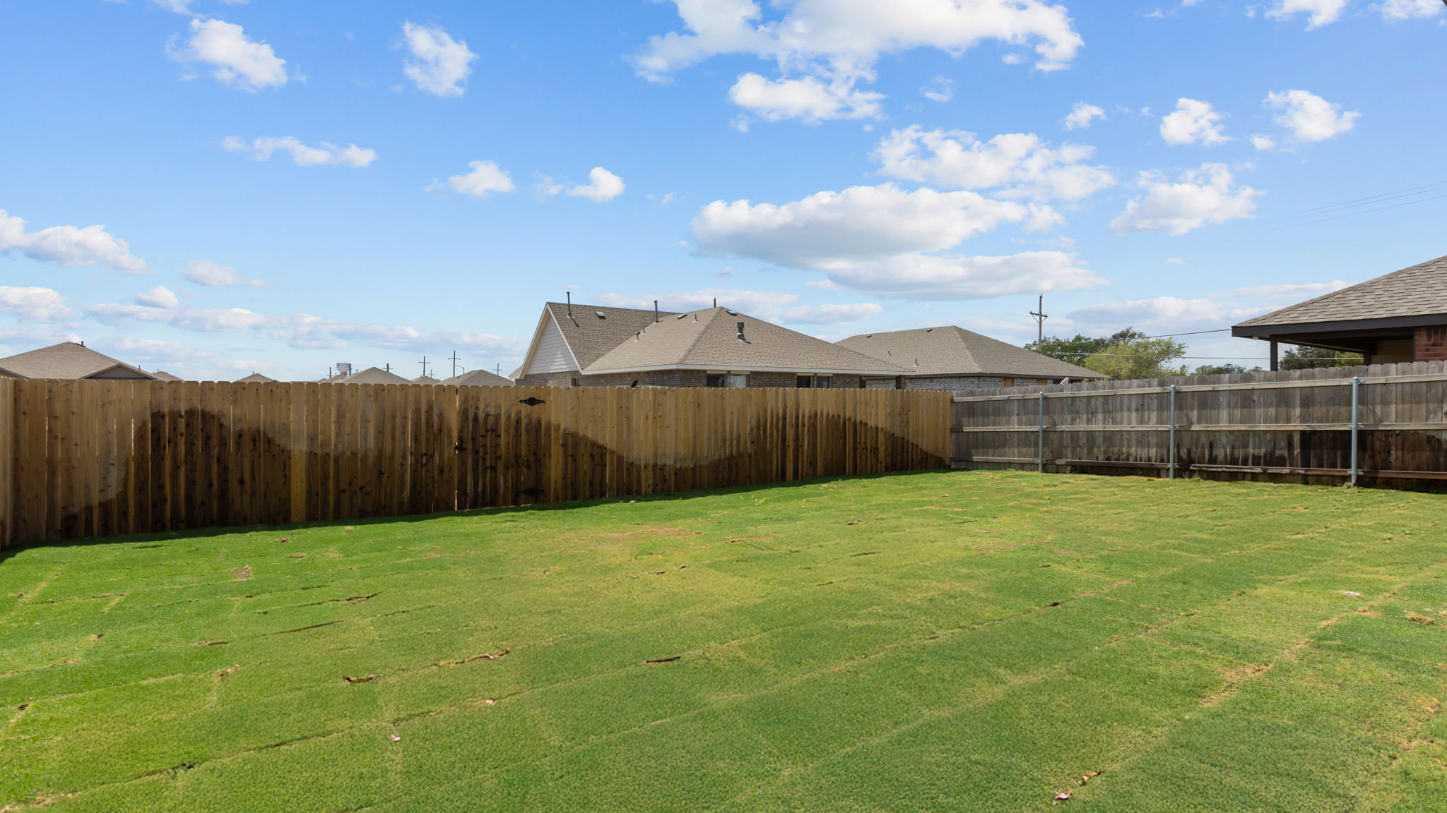 Spacious backyard with plush green grass, privacy fence, and covered patio