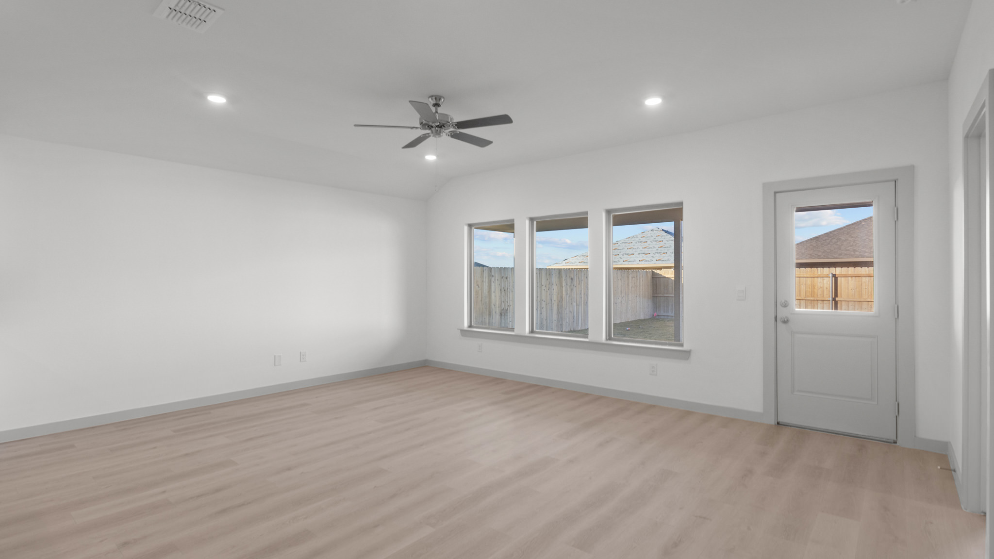 Open airy family room with vinyl plank flooring and windows overlooking backyard