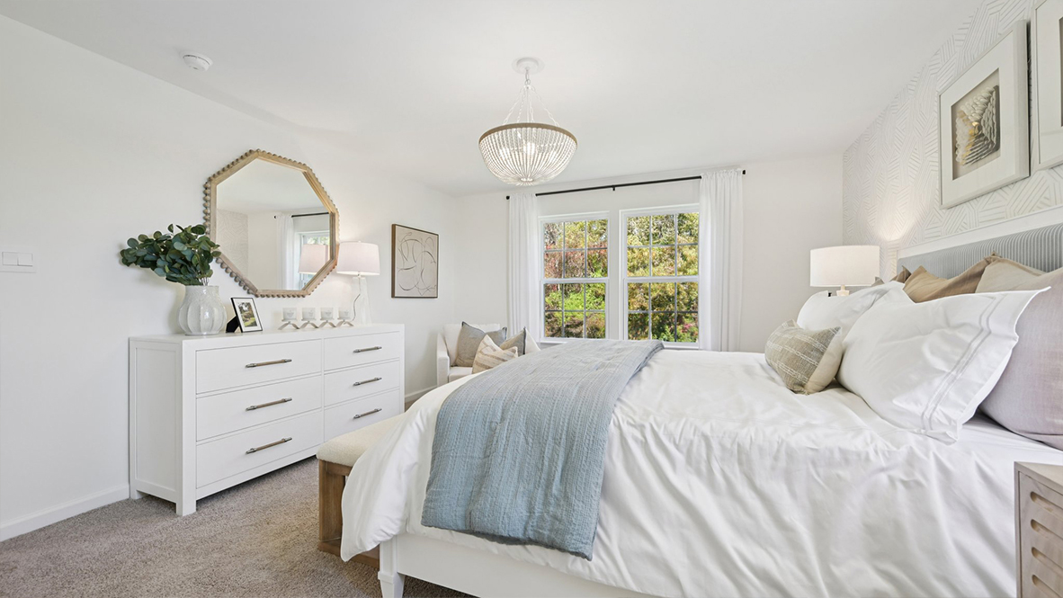 spacious primary suite with neutral tones throughout, large windows, and a beautiful light fixture