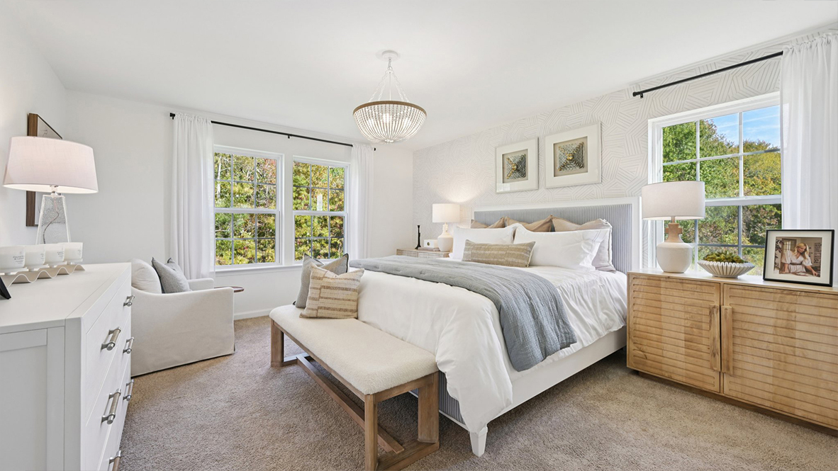 spacious primary suite with neutral tones throughout, large windows, and a beautiful light fixture