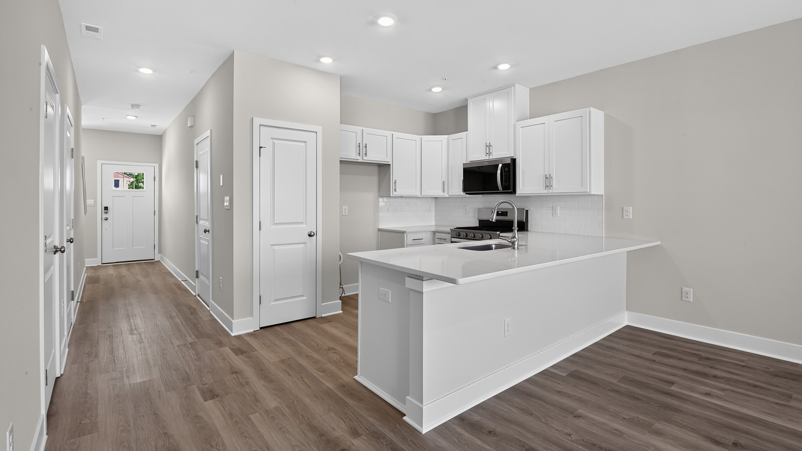 modern front entrance and spacious kitchen in the delmar model,featuring a quartz countertop, white cabinetry and stainless steel appliances