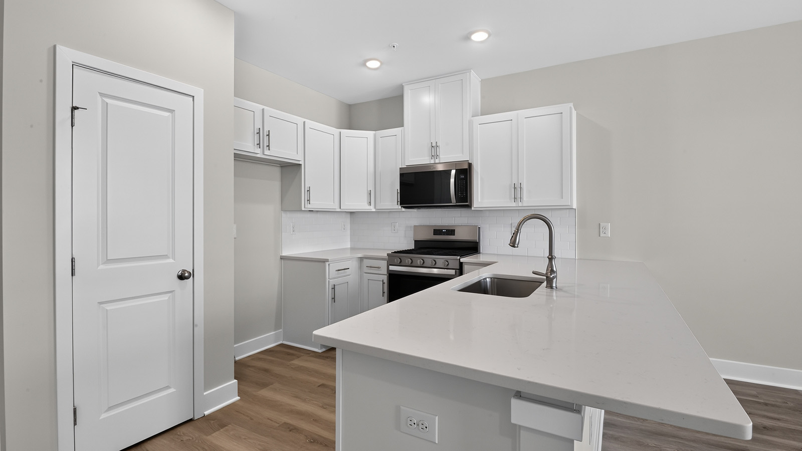 modern front entrance and spacious kitchen in the delmar model,featuring a quartz countertop, white cabinetry and stainless steel appliances