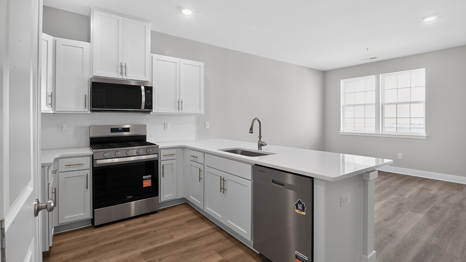 modern front entrance and spacious kitchen in the delmar model,featuring a quartz countertop, white cabinetry and stainless steel appliances