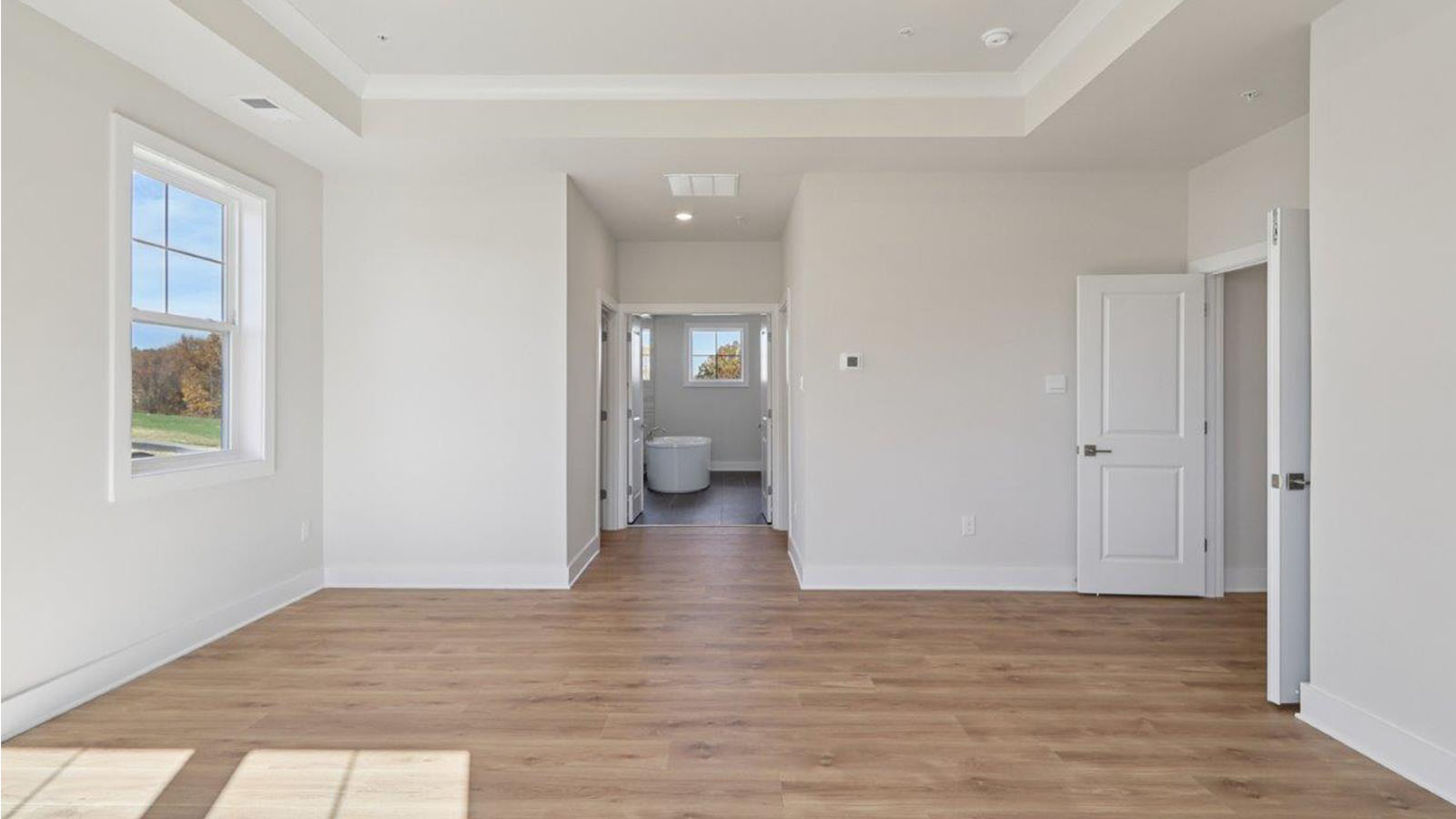 spacious primary suite with medium hardwood floors and large windows