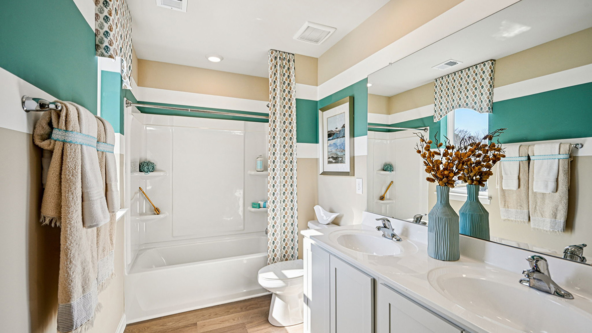 A guest bathroom has a double-bowl vanity, toilet, and shower tub.