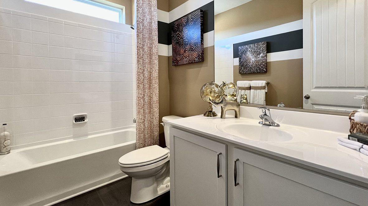 Inside the guest bathroom, there is a vanity, toilet, and a large window above the shower.